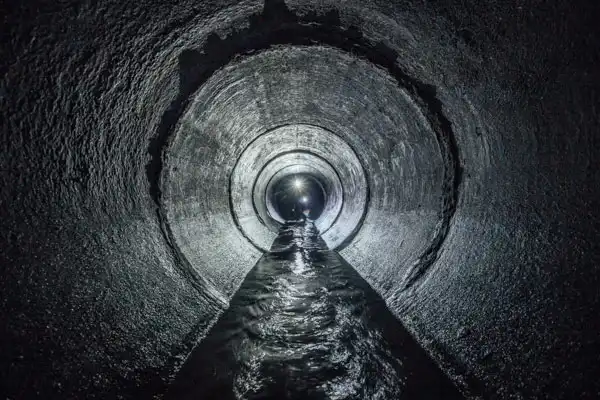 Inside view of a large, circular concrete sewer tunnel in Boston, MA, with water flowing along the bottom—a testament to advanced trenchless sewer line installation—light is visible at the far end.