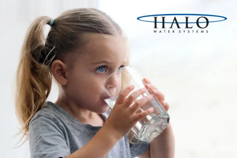 A young girl with a ponytail drinks a glass of water, purified by a Water Filtration System. The HALO Water Systems logo appears in the top right corner.