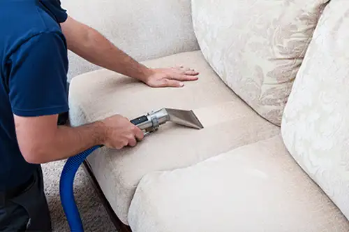 Person cleaning couch with vacuum cleaner nozzle.