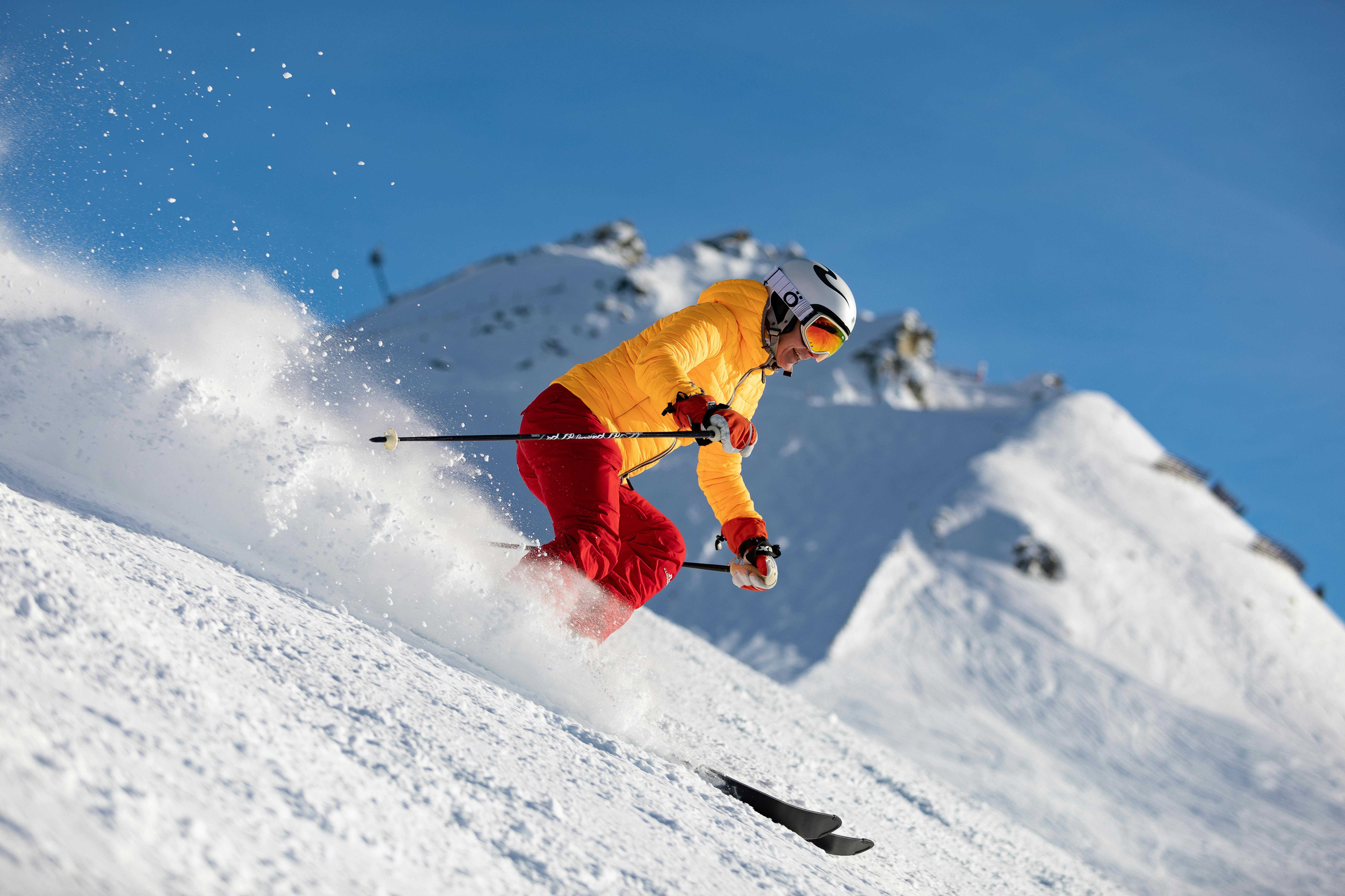 Dynamic skier in bright yellow jacket and red pants enjoying winter sports on snowy mountain slope beneath clear blue sky at Bay-O-Vista Swim & Tennis Club.