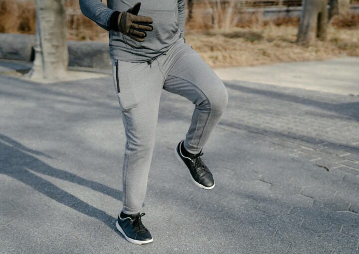 Running man in athletic wear jogging outdoors on paved pathway, fitness and active lifestyle, exercise, gym, outdoor workout, sports, health and wellness, urban jogging scene, cold weather gear, sports shoes.