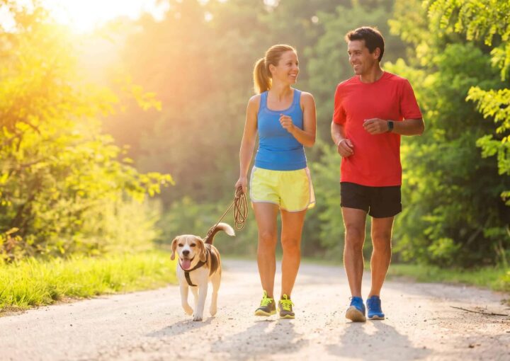 Happy couple jogging with their dog on a scenic trail at Bay-O-Vista Swim & Tennis Club during spring, promoting outdoor fitness and community activities.