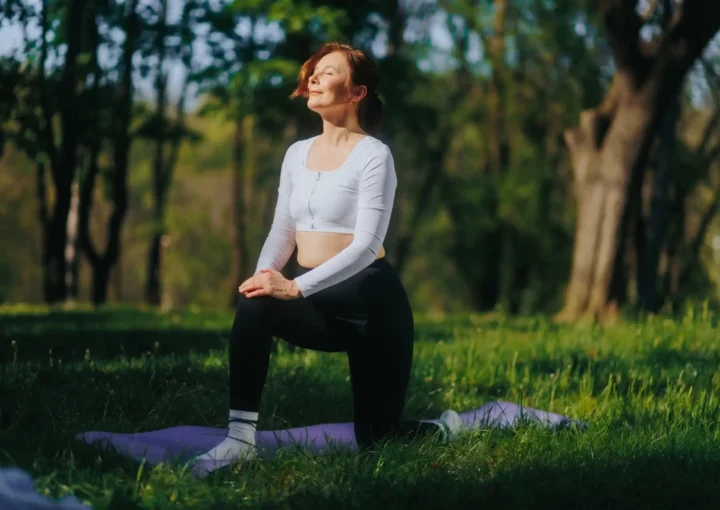 Woman practicing yoga outdoors in a park during summer, promoting fitness and wellness.