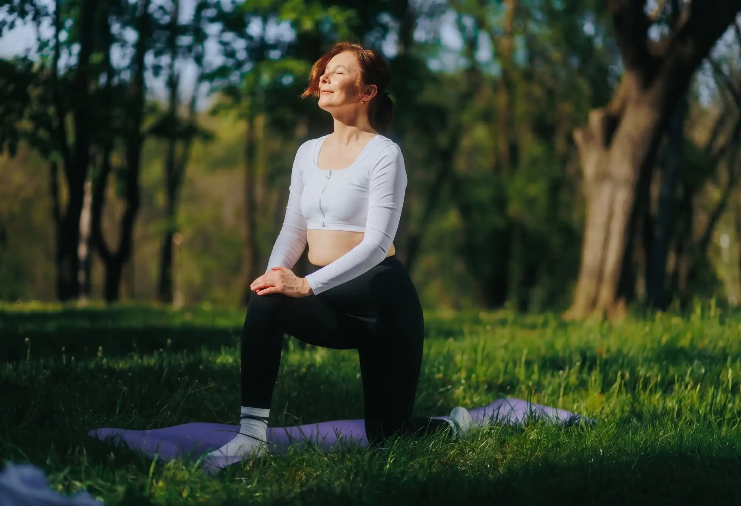 Woman practicing yoga outdoors in a park during summer, promoting fitness and wellness.
