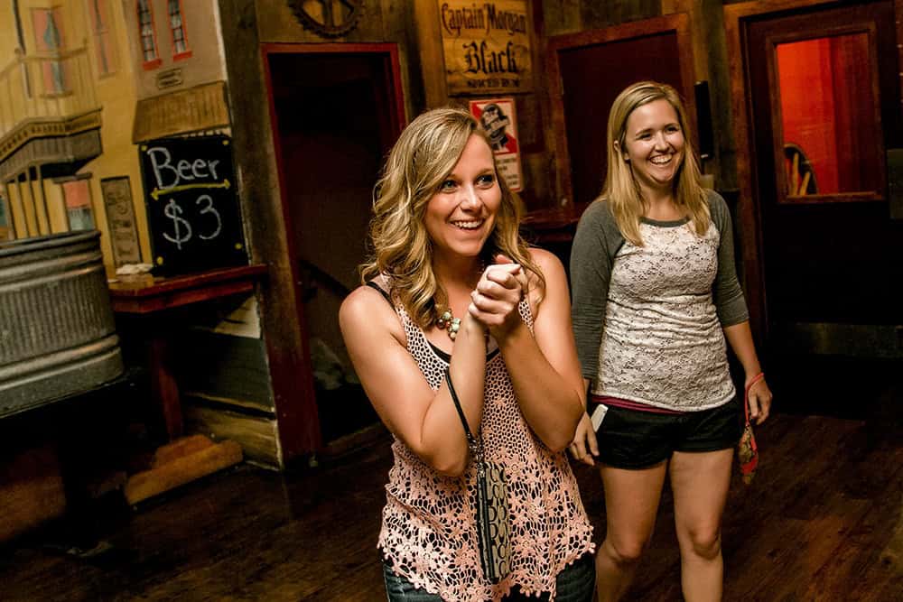 Two women exchange a surprise proposal amidst joyful cheers at a bar, clutching a wii remote.