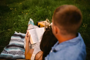 A person reads a book while leaning against another on a blanket in the grass, capturing a candid moment reminiscent of an Eau Claire Wedding Photographer’s romantic style.