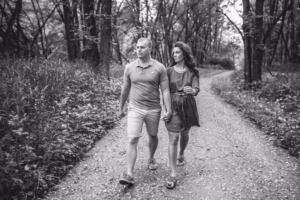 A man and woman walk arm-in-arm down a wooded path. Captured in timeless black and white, this moment reflects the artistry of an Eau Claire Wedding Photographer.