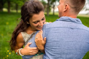 A woman smiles and holds a man's arm while standing outside on a grassy area, beautifully captured by an Eau Claire wedding photographer.