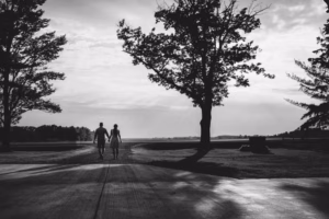 A couple walks hand in hand down a paved path lined with trees, silhouetted against a cloudy sky—captured beautifully by an Eau Claire wedding photographer.