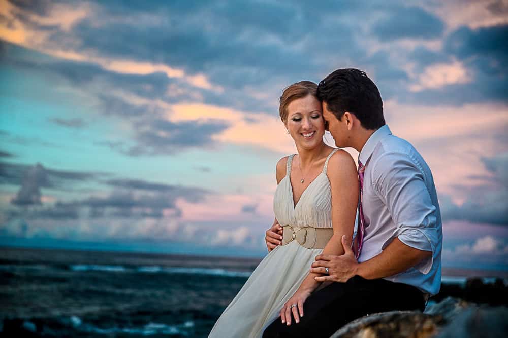 Beautiful wedding couple sitting on rocks at sunset.