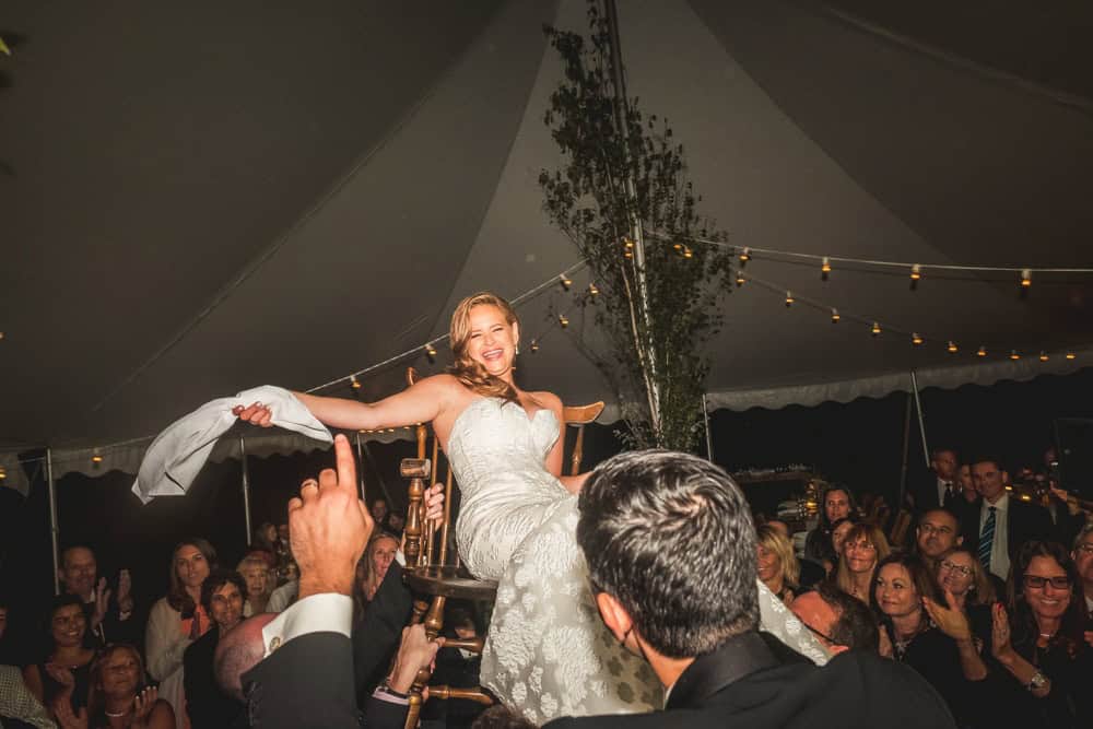 A Jewish bride in a wedding dress is being carried by her guests.