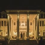A bride and groom captured by a skilled Littleton Wedding Photographer in front of a large mansion at night.