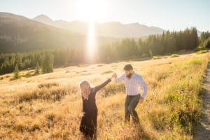 A couple is walking through a grassy field during their Boreas Pass engagement session.
