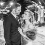 A couple embraces in front of Christmas lights at their dog wedding celebration.
