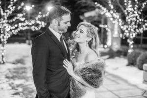 A couple embraces in front of Christmas lights at their dog wedding celebration.