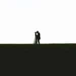 A silhouette of a bride and groom on a grassy field.