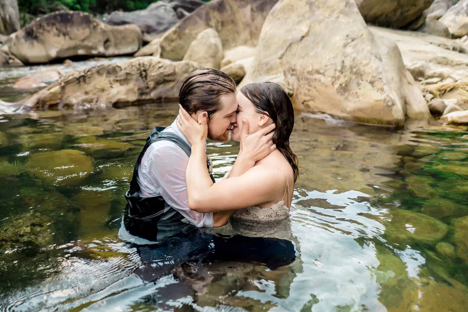 A bride and groom kissing in the water of a river.