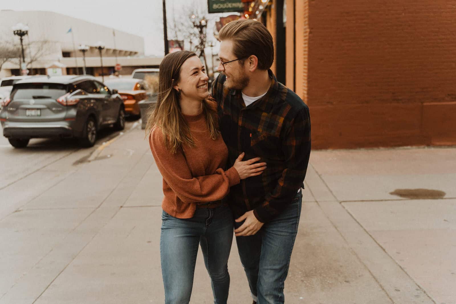 A couple laughing on the sidewalk during their engagement session.