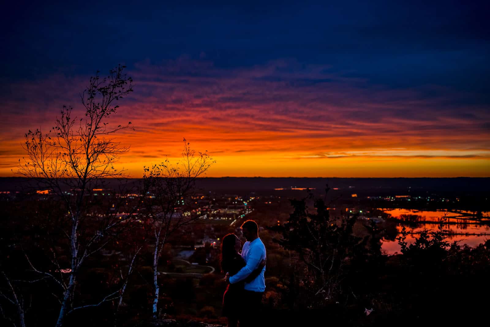 A couple standing on top of a hill with a sunset in the background.