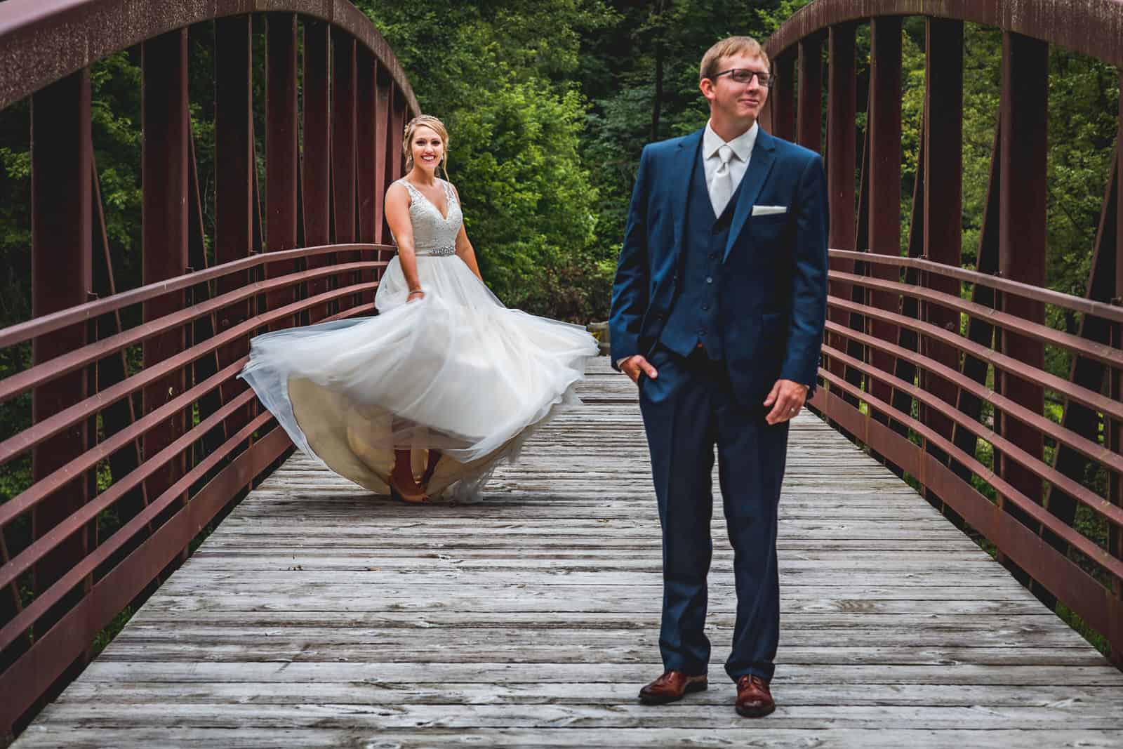 A bride and groom standing on a wooden bridge.