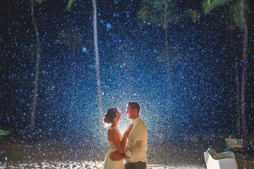 A bride and groom standing under a waterfall at night.