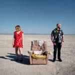 A man and woman standing next to a chair in the desert.
