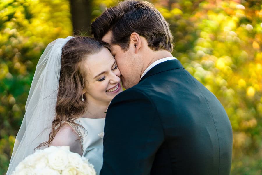 A bride and groom embracing in the fall.