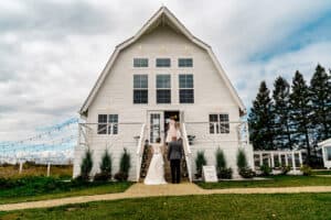 A bride and groom standing outside of a white barn.