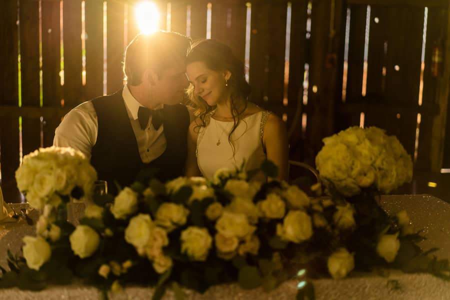 A bride and groom sitting at a table in a barn.