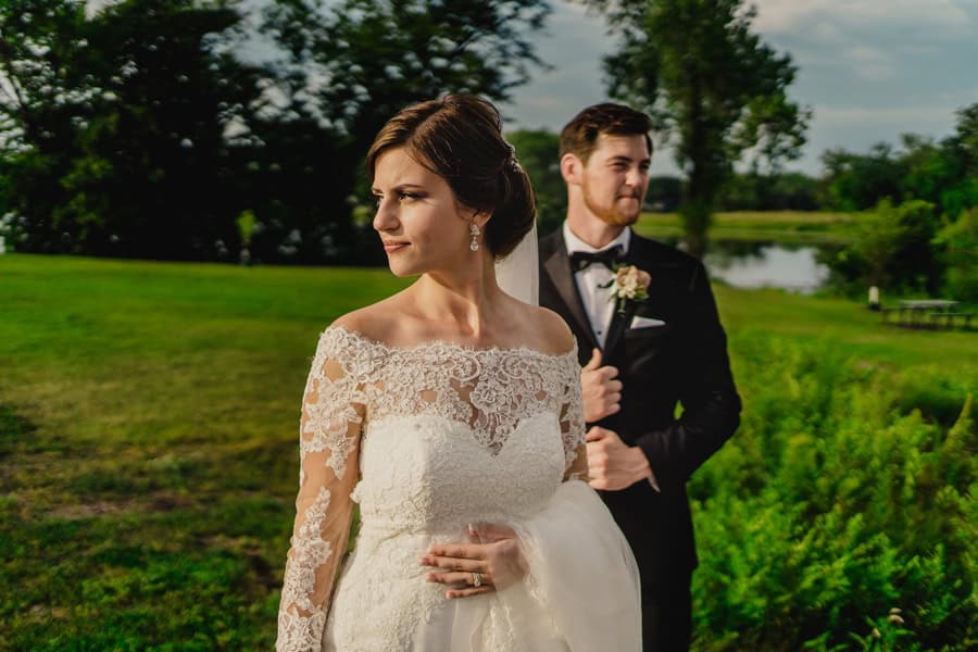 A bride and groom standing in front of a pond.