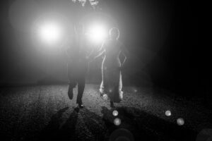 A bride and groom walking down a dark road at night.