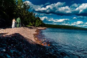 A bride and groom standing on the shore of a lake.