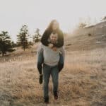A man is carrying a woman in a field at sunset.