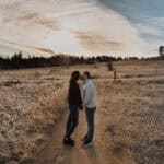 A couple standing on a path in a field at sunset.