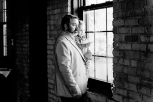 A man with a beard standing by a window.