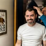 A man with a beard is getting his hair done in a love-filled backyard.