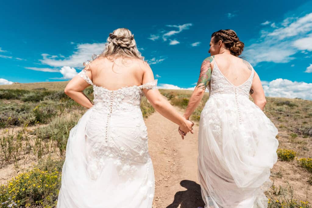 gay couples takes photos on peak of granby lake co002 Two brides walking down a dirt road holding hands.