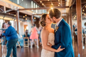 A bride and groom share a kiss on the dance floor during their wedding reception in a warmly lit venue, with guests in the background—one of many magical moments at Colorado Parks wedding venues.