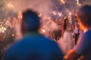 A bride and groom walk through a crowd holding sparklers at night, with smoke and people blurred in the foreground—capturing the magic of Colorado Parks wedding venues.