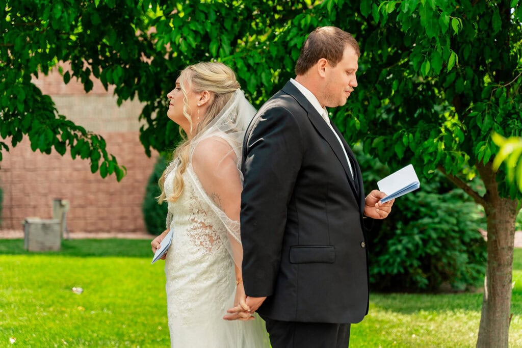 emily-patrick-private-first-touch-vow-exchange-maple-grove-events.jpg Bride and groom stand back-to-back outdoors during wedding ceremony at Maple Grove Events.
