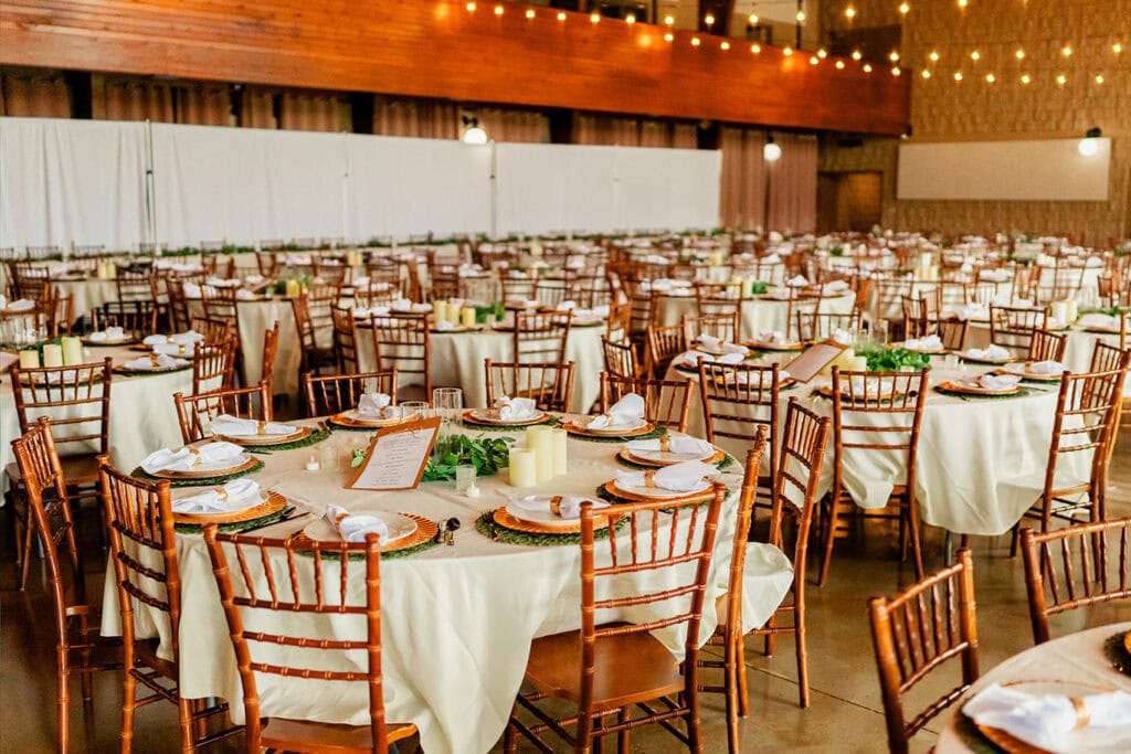 maple-grove-events-west-salem-wi-wedding-reception-hall-setup.jpg Elegant wedding reception setup with round tables, white tablecloths, and wooden chairs at Maple Grove Events.