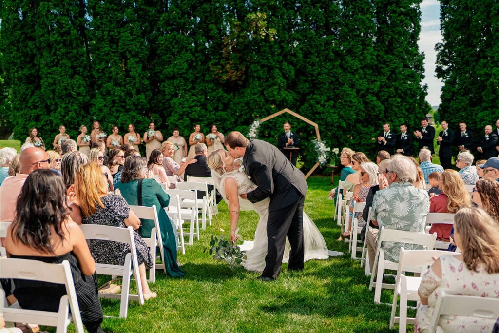 outdoor-wedding-ceremony-lawn-maple-grove-events-west-salem-wi.jpg Wedding ceremony at Maple Grove Events with guests seated on white chairs and a couple exchanging vows outdoors.