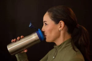 Woman drinking water from a stainless steel bottle, promoting hydration and tongue posture.