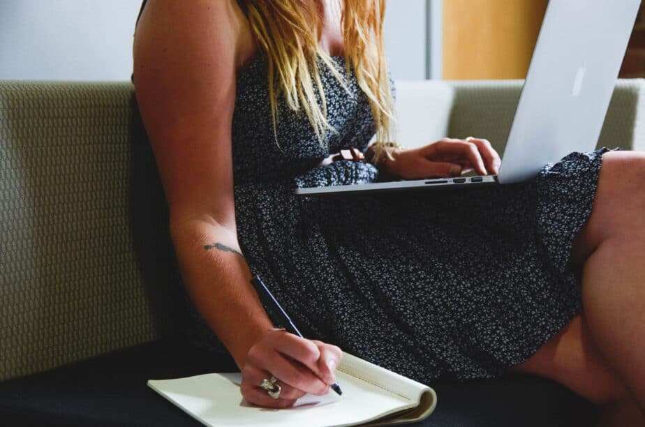 An image at at brianvanderwaal.com/personal-profile-for-cv of a woman writing a personal profile for CV with her right hand in a notebook whilst holding a laptop in her lap.