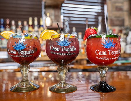 Three colorful cocktails with fruit garnishes on a bar counter at Casa Tequila.