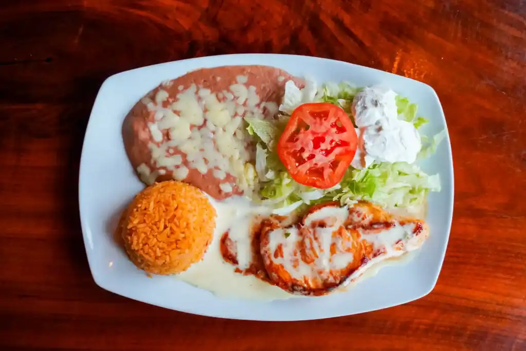 Traditional Mexican dish with rice, salad, and grilled chicken on a white plate.