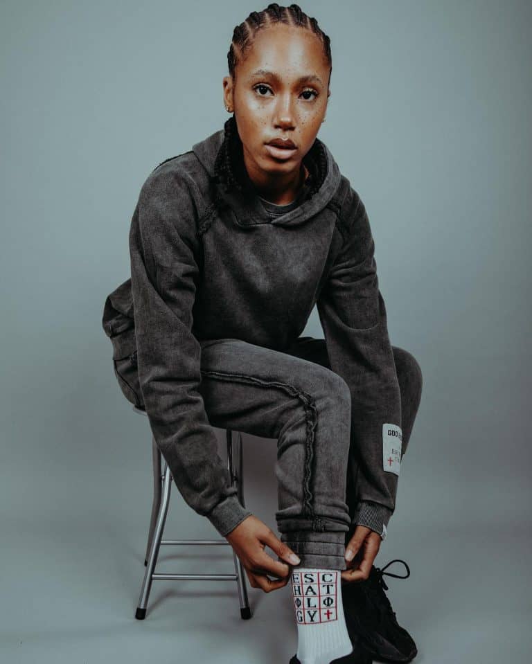 Young woman in black streetwear hoodie and joggers sitting on a chair.