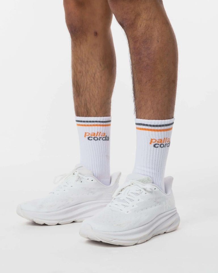 Close-up of men's white sneakers and socks on a plain background.