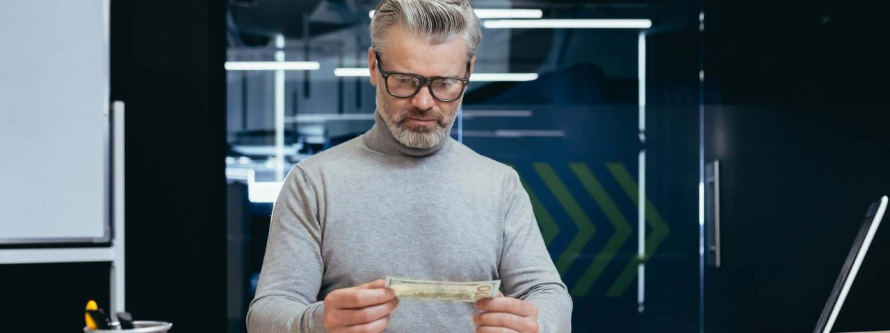 Dissatisfied and disappointed businessman inside office looking at his salary and income, mature