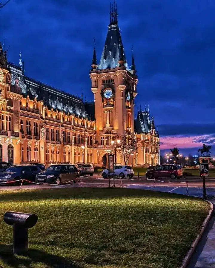Castle-style historic building illuminated at dusk, with parked cars in front.